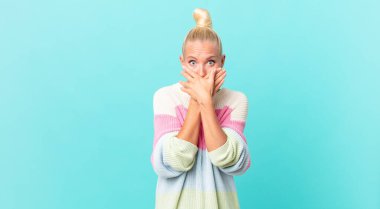 Güzel sarışın kadın, elleri ve ağzı şoka uğramış bir şekilde kapatıyor.