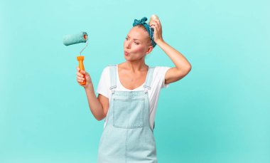 Güzel sarışın kadın şaşkın ve şaşkın hissediyor, kafasını kaşıyor ve bir duvar boyuyor.