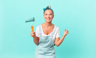 Güzel sarışın kadın şokta, gülüyor, başarıyı kutluyor ve duvar boyuyor.