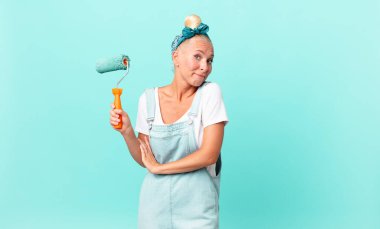 Güzel sarışın kadın omuz silkiyor, kafası karışık ve kararsız ve duvar boyuyor.