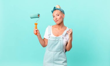 Güzel sarışın kadın kibirli, başarılı, pozitif ve gururlu görünüyor ve bir duvar boyuyor.