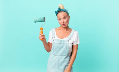 Güzel sarışın kadın şaşkın ve şaşkın hissediyor ve bir duvar boyuyor.