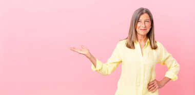 Güzel orta yaşlı bir kadın mutlu bir şekilde gülümsüyor, eli kalçasında ve kendinden emin.