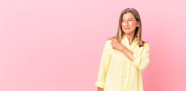 Güzel orta yaşlı bir kadın neşeli bir şekilde gülümsüyor, mutlu hissediyor ve bir tarafa işaret ediyor.