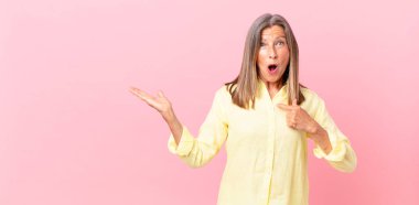 Oldukça orta yaşlı bir kadın şok olmuş ve şaşırmış görünüyor ağzı açık, kendini işaret ediyor.