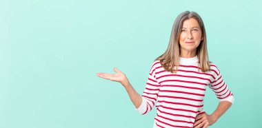 Güzel orta yaşlı bir kadın mutlu bir şekilde gülümsüyor, eli kalçasında ve kendinden emin.