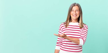 Güzel orta yaşlı bir kadın neşeli bir şekilde gülümsüyor, mutlu hissediyor ve bir konsept gösteriyor.