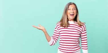 Güzel orta yaşlı bir kadın mutlu ve hoş bir şekilde şaşırmış görünüyor.