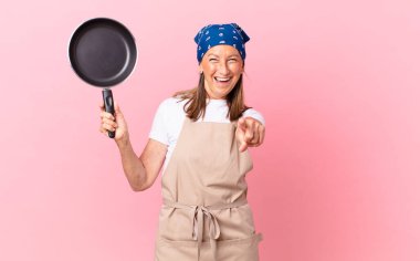 Kamerayı işaret eden orta yaşlı bir kadın seni seçiyor ve elinde bir tava tutuyor. Şef konsepti