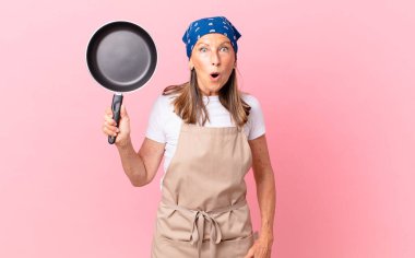 Oldukça orta yaşlı bir kadın şok olmuş ya da şaşırmış görünüyor ve elinde bir tava tutuyor. Şef konsepti