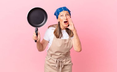 Orta yaşlı güzel bir kadın mutlu hissediyordu, elleri ağızının yanında ve elinde bir tavayla bağırıyordu. Şef konsepti