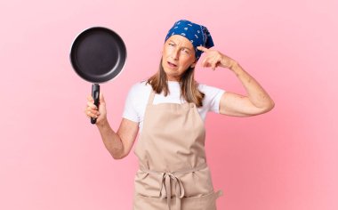 Oldukça orta yaşlı bir kadın kafası karışık ve şaşkın hissediyor, deli olduğunu ve elinde bir tava tuttuğunu gösteriyor. Şef konsepti