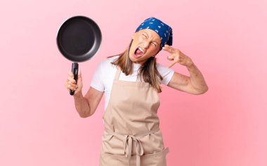 Oldukça orta yaşlı bir kadın mutsuz ve stresli görünüyor, intihar jesti silah işareti yapıyor ve elinde bir tava tutuyor. Şef konsepti