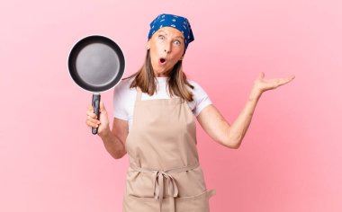 Oldukça orta yaşlı bir kadın şaşırmış ve şok olmuş görünüyor. Çenesi düşmüş, elinde bir nesne, elinde bir tavayla. Şef konsepti