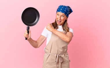 Orta yaşlı güzel bir kadın kendini mutlu hissediyor ve bir meydan okumayla yüzleşiyor ya da kutluyor ve elinde bir tava tutuyor. Şef konsepti