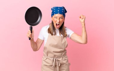 Oldukça orta yaşlı bir kadın sinirli bir ifadeyle bağırıyor ve elinde bir tavayla. Şef konsepti