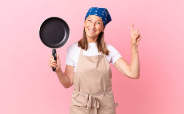 Güzel, orta yaşlı bir kadın bir fikri fark ettikten ve elinde tavayla gezdikten sonra mutlu ve heyecanlı bir dahi gibi hissediyor. Şef konsepti