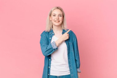 Sarışın, güzel bir kadın neşeli bir şekilde gülümsüyor, mutlu hissediyor ve bir tarafı işaret ediyor.