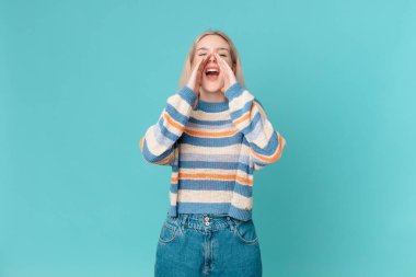 Sarışın, güzel bir kadın kendini mutlu hissediyor. Elleri ağızda, kocaman bağırıyor.