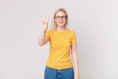 Güzel sarışın kadın gülümsüyor ve mutlu görünüyor, zafer ya da barış işareti yapıyor.