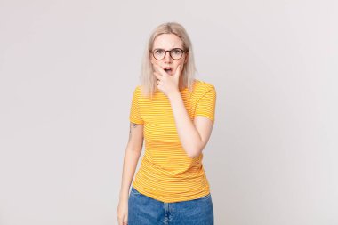 Sarışın, güzel bir kadın, ağzı ve gözleri açık, elleri çenesinde.