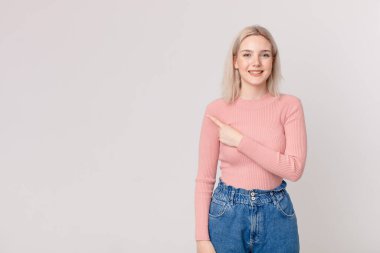 Sarışın, güzel bir kadın neşeli bir şekilde gülümsüyor, mutlu hissediyor ve bir tarafı işaret ediyor.