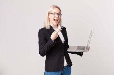 Sarışın, güzel bir kadın heyecanlı ve şaşırmış görünüyor. Yan tarafı gösteriyor ve elinde dizüstü bilgisayar var.