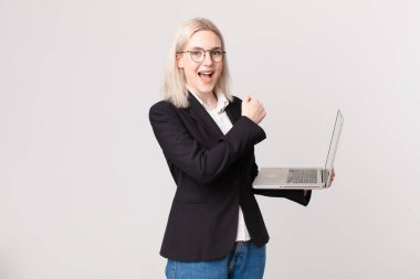 Sarışın, güzel bir kadın mutlu ve zorluklarla yüzleşiyor ya da kutlama yapıyor ve dizüstü bilgisayar tutuyor.