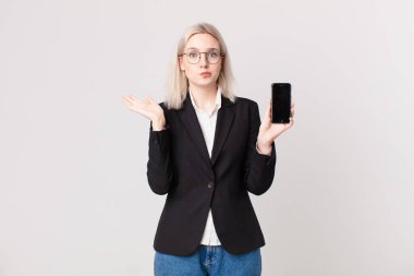 Sarışın, güzel bir kadın şaşkın, şaşkın, şüpheci ve elinde bir cep telefonu tutuyor.