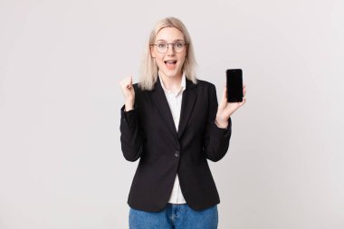Sarışın, güzel bir kadın şoke olmuş, gülüyor, başarıyı kutluyor ve elinde bir cep telefonu tutuyor.