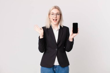 Sarışın, güzel bir kadın kendini mutlu ve şaşkın hissediyor. İnanılmaz bir şey ve bir cep telefonu tutuyor.