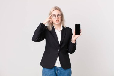 Sarışın, güzel bir kadın şaşkın ve şaşkın hissediyor, deli olduğunu ve elinde cep telefonu tuttuğunu gösteriyor.