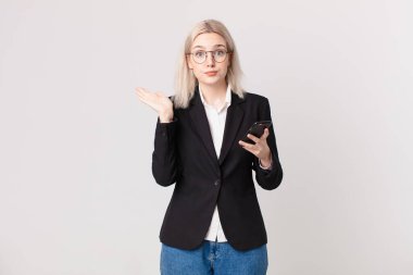 Sarışın, güzel bir kadın şaşkın, şaşkın, şüpheci ve elinde bir cep telefonu tutuyor.