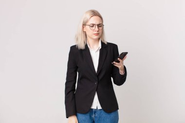 Sarışın, güzel bir kadın üzgün, üzgün ya da kızgın ve yana bakıyor ve elinde bir cep telefonu tutuyor.