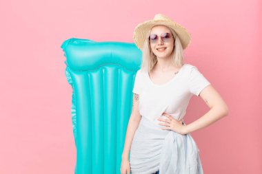 Sarışın, güzel bir kadın mutlu bir şekilde gülümsüyor, eli kalçasında ve kendinden emin. yaz konsepti