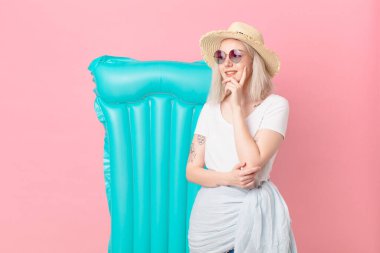 Sarışın, güzel bir kadın mutlu bir şekilde gülümsüyor ve hayal kuruyor ya da şüphe ediyor. yaz konsepti