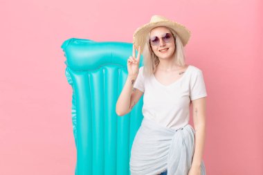 Sarışın, güzel bir kadın gülümsüyor ve arkadaş canlısı görünüyor. İki numarayı gösteriyor. yaz konsepti