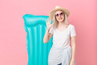 Sarışın, güzel bir kadın gülümsüyor ve arkadaş canlısı görünüyor. Beş numarayı gösteriyor. yaz konsepti