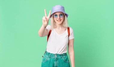 Gülümseyen ve mutlu görünen sarışın güzel kadın zafer ya da huzur işareti yapıyor. yaz konsepti