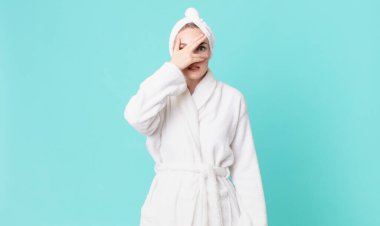 Sarışın, güzel bir kadın. Şok olmuş, korkmuş ya da korkmuş görünüyor. Yüzü elle örtülmüş ve bornoz giyiyor.