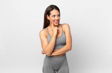 Genç İspanyol kadın mutlu bir şekilde gülümsüyor ve hayal kuruyor ya da şüphe ediyor. fitness konsepti