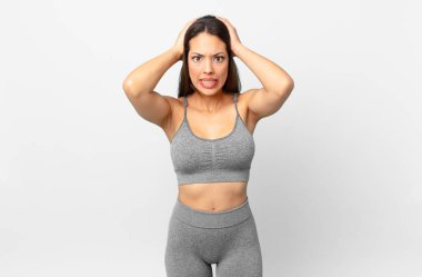 Genç İspanyol kadın stresli, endişeli ya da korkmuş hissediyor, elleri başının üstünde. fitness konsepti