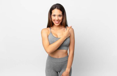 Genç İspanyol kadın neşeyle gülümsüyor, mutlu hissediyor ve bir tarafı işaret ediyor. fitness konsepti