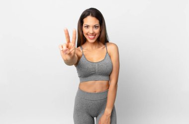 Genç İspanyol kadın gülümsüyor ve arkadaş canlısı görünüyor, iki numarayı gösteriyor. fitness konsepti