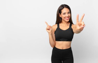 Genç İspanyol kadın gülümsüyor ve arkadaş canlısı görünüyor, iki numarayı gösteriyor. fitness konsepti