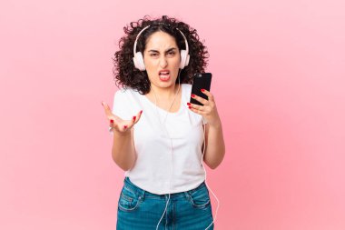 Güzel bir Arap kadını sinirli, sinirli ve hayal kırıklığına uğramış bir kulaklık ve akıllı bir telefon ile