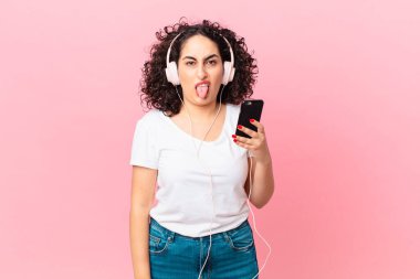 Güzel bir Arap kadın, tiksinmiş ve rahatsız olmuş hissediyor. Kulaklıkla ve akıllı telefonuyla dilini çıkarıyor.