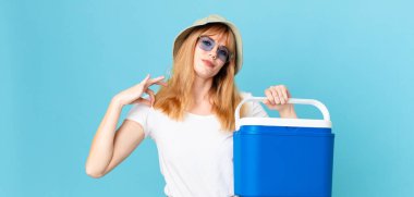 Güzel kızıl saçlı kadın kibirli, başarılı, pozitif ve gururlu görünüyor ve portatif bir buzdolabı tutuyor. yaz konsepti