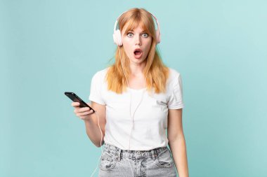 Güzel kızıl saçlı kadın çok şaşırmış görünüyor ve kulaklıkla müzik dinliyor.