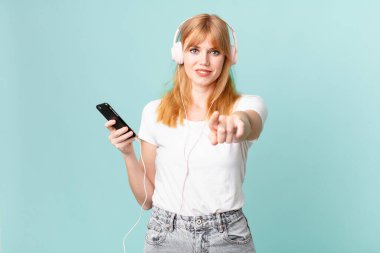Güzel kızıl saçlı kadın kamerayı işaret ederek seni seçiyor ve kulaklıkla müzik dinliyor.